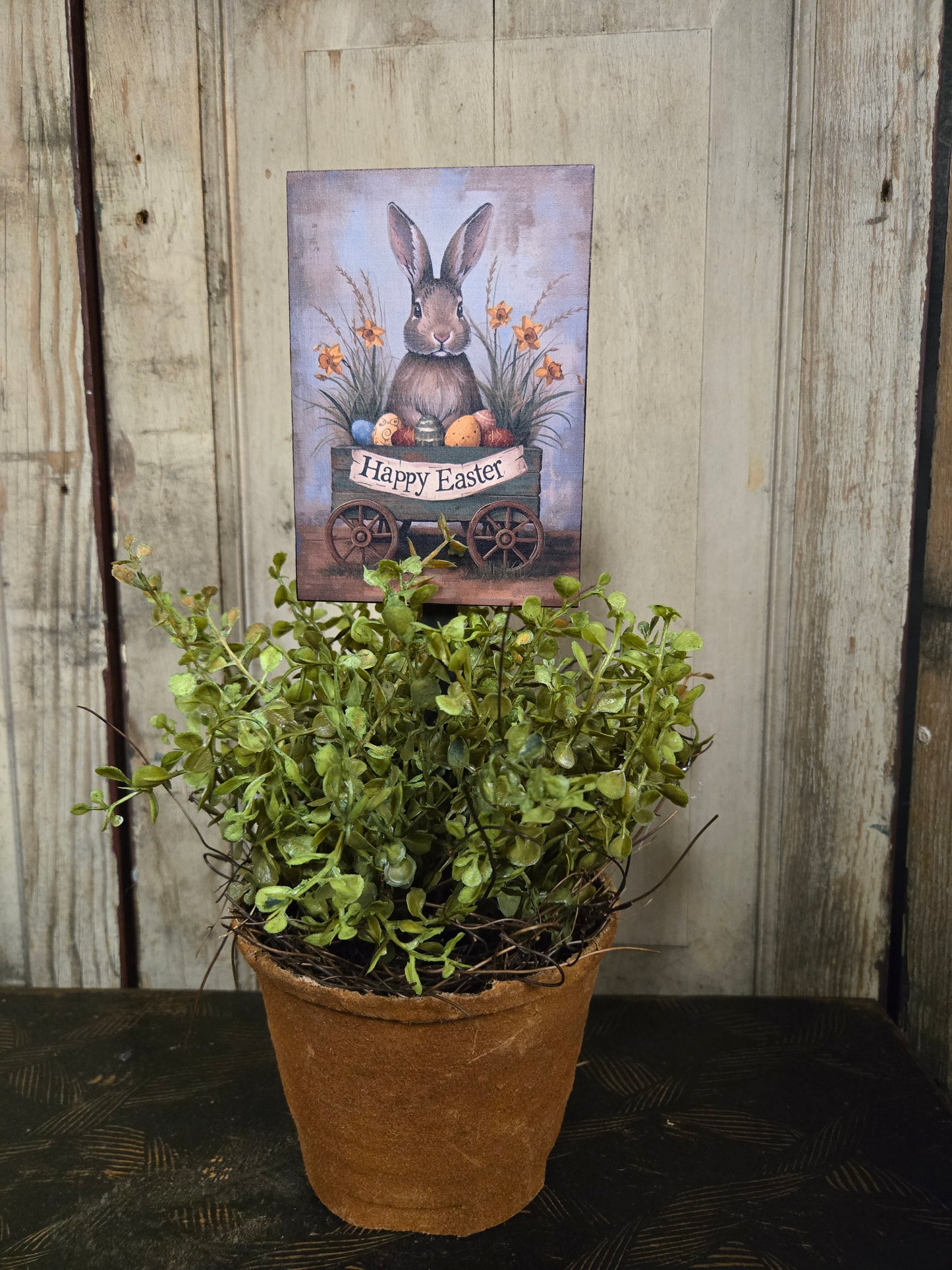 Potted plant on a wooden surface with a Easter-themed card in the background
