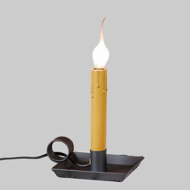 A square pan window light with a smokey black finish, featuring a candle-like bulb glowing on a windowsill.