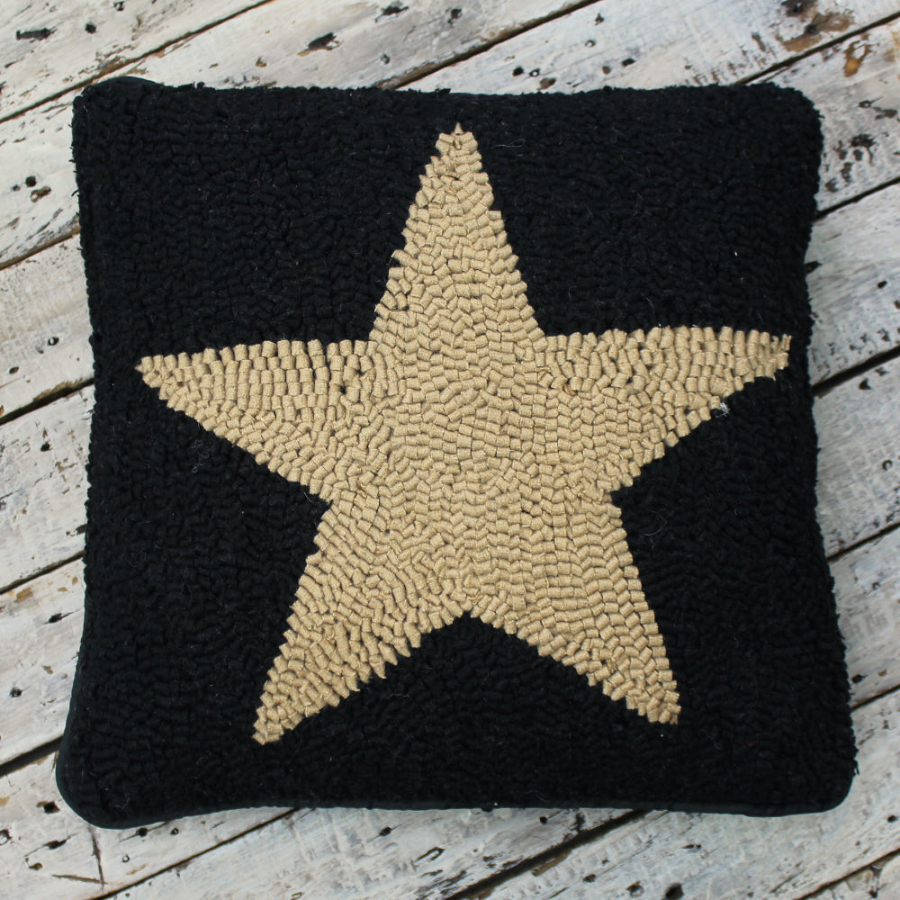 A square-shaped throw pillow with a black background and a large star-shaped pattern in a neutral color on the star's border.