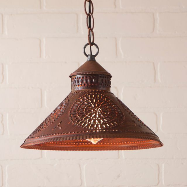 Decorative rustic tin pendant light with chisel design against a white brick wall