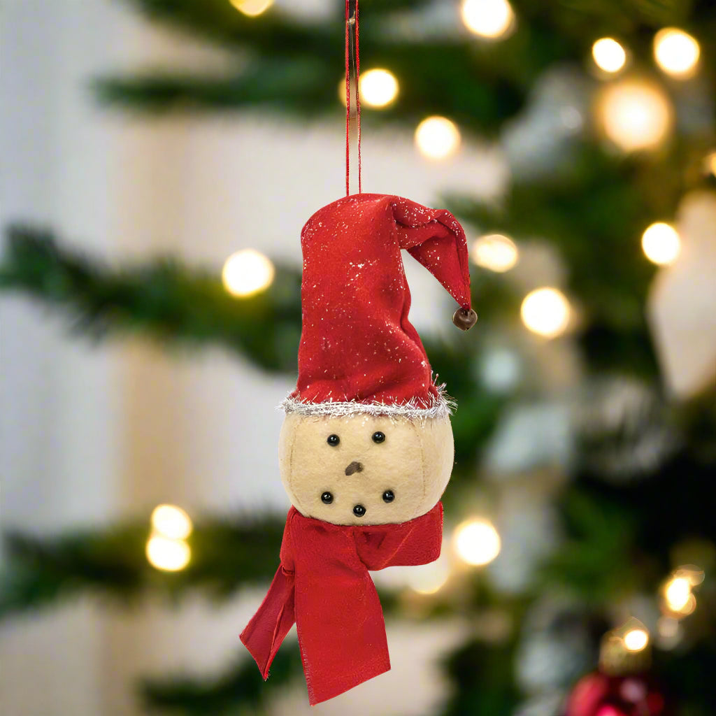 A plush snowman head ornament with a red fabric scarf and stocking cap, hanging from a fabric string.