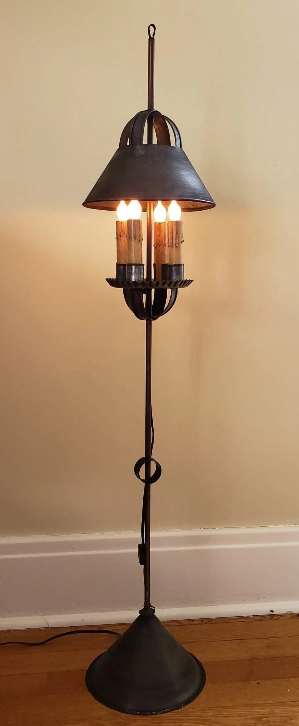 A Stratton Mini Tin Floor Lamp with a rustic, primitive finish, featuring a black lamp post and a round metal shade with two visible bulb sockets.