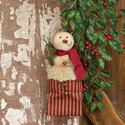 Decorative snowman with a red scarf and striped pants hanging on a wooden door with greenery.