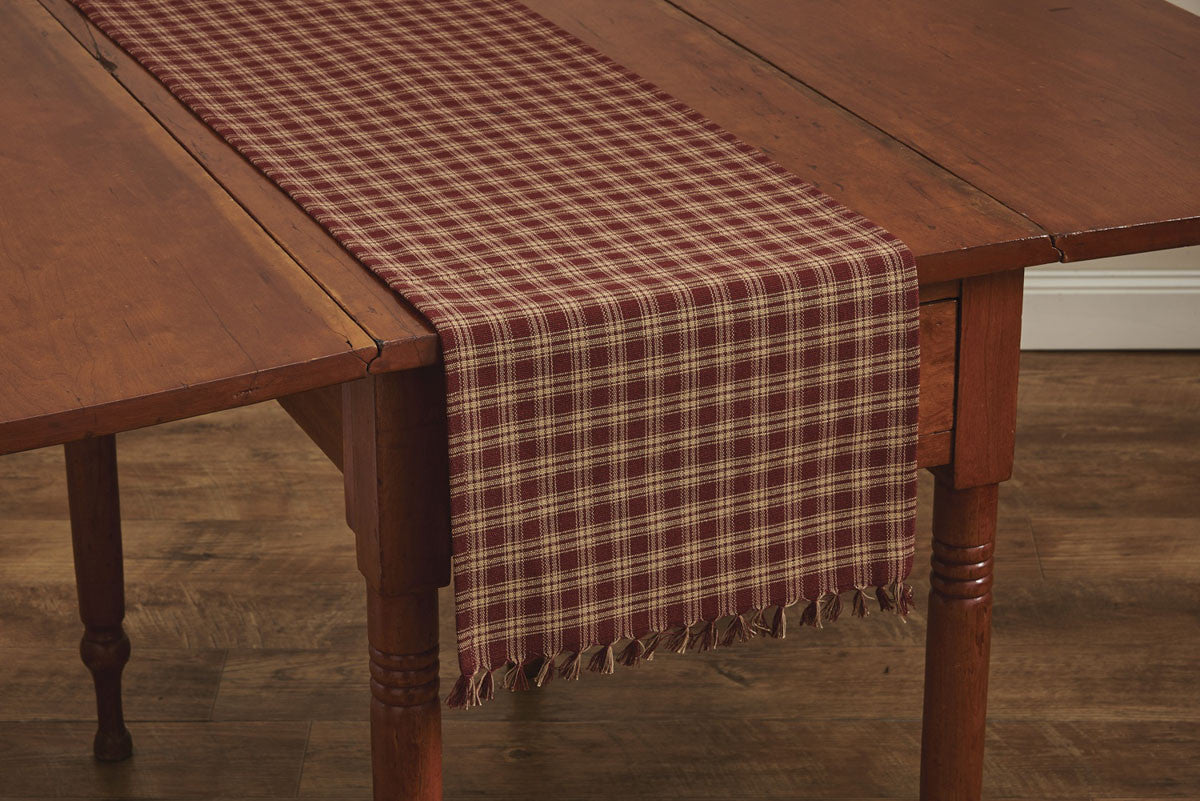 A wine-colored checkered table runner with a fringed edge laid out on a wooden dining table.