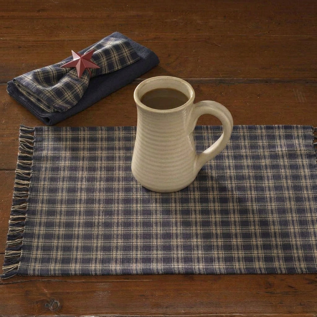 Table setting with a plaid runner, mug, plates with bread, and a candle.