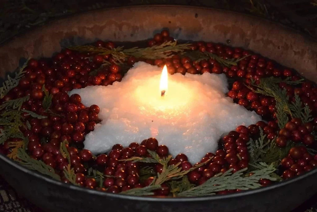 Lit white star-shaped Sugar Cookie floating candle in a rustic metal bowl, surrounded by red berries and evergreen sprigs