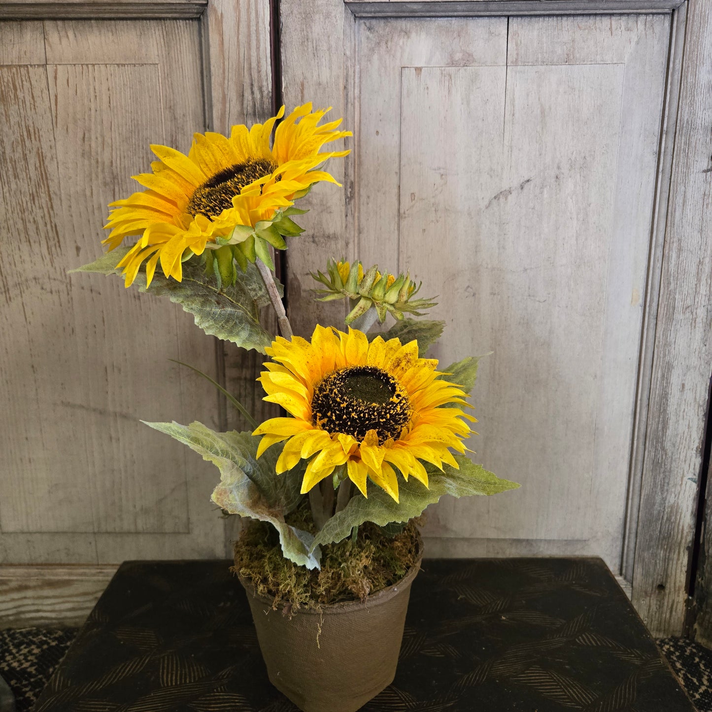 Two artificial sunflowers on a rustic wooden surface