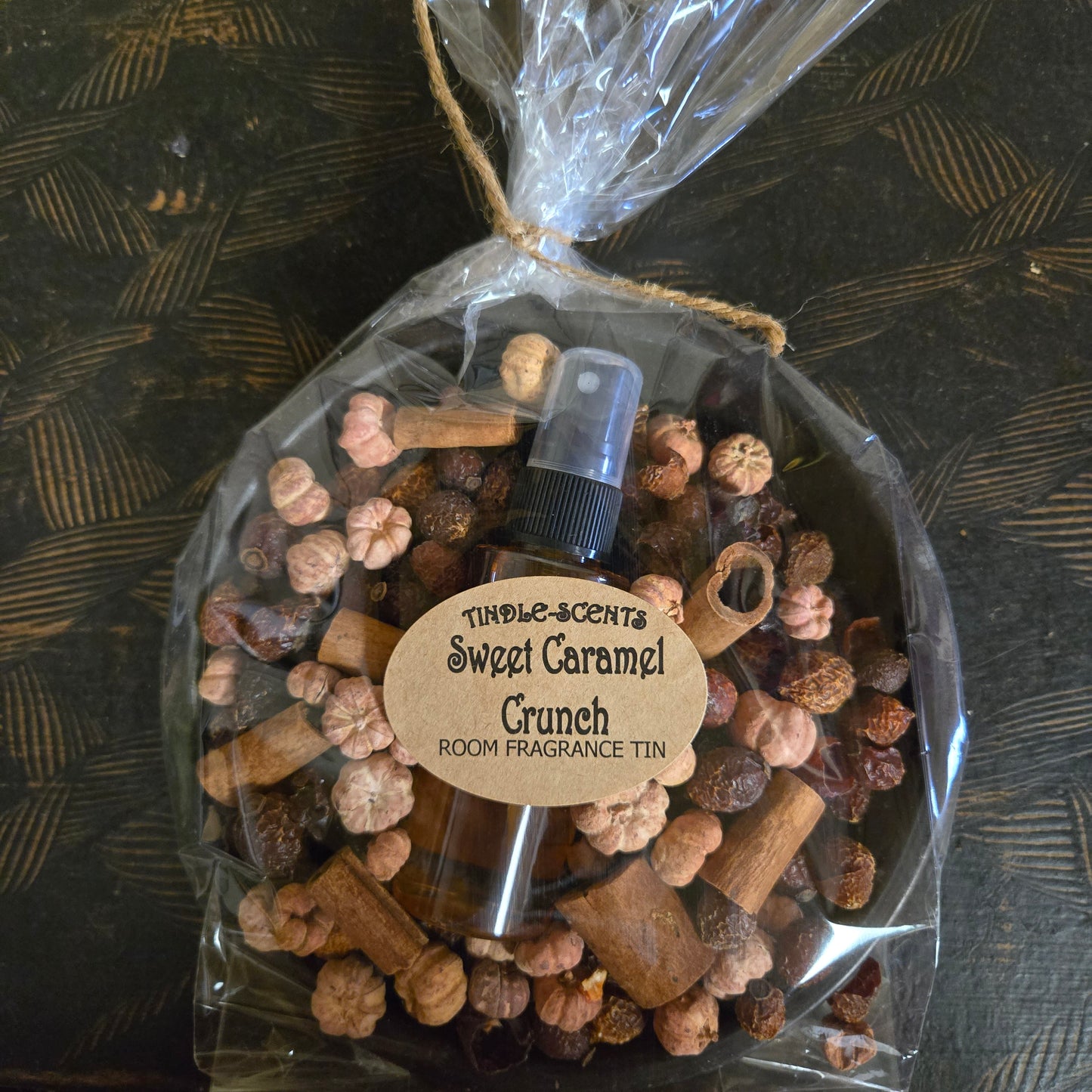 Room fragrance tin labeled 'Sweet Caramel Crunch' with decorative elements on a textured surface.