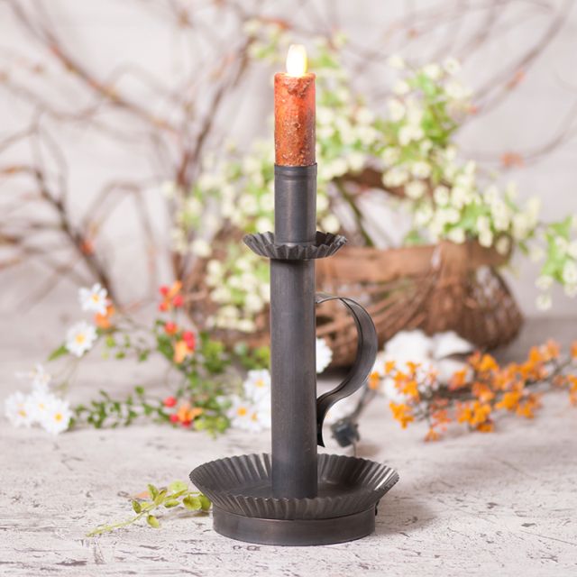 Decorative candle holder with a lit candle on a rustic surface with flowers in the background