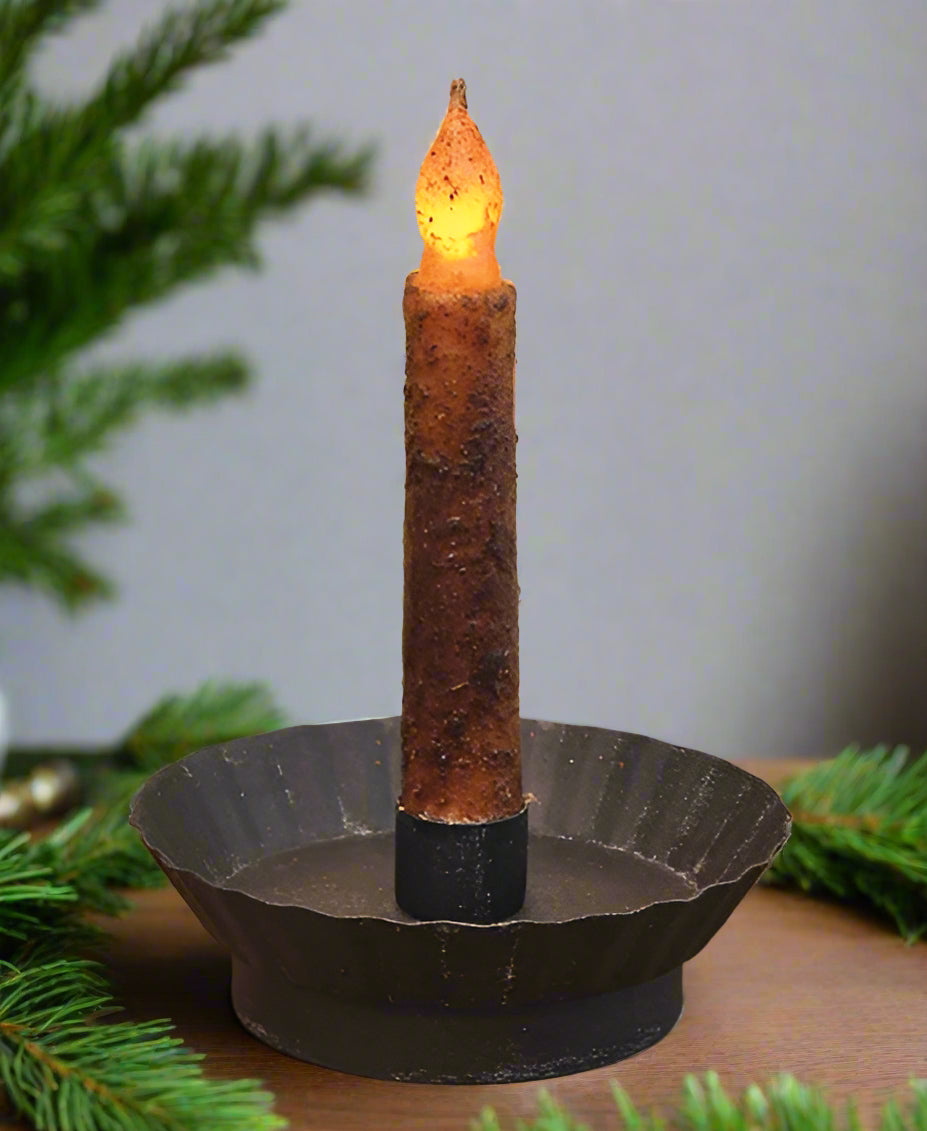 A black metal taper candle holder with a fluted design and a lit candle, set on a wooden surface.