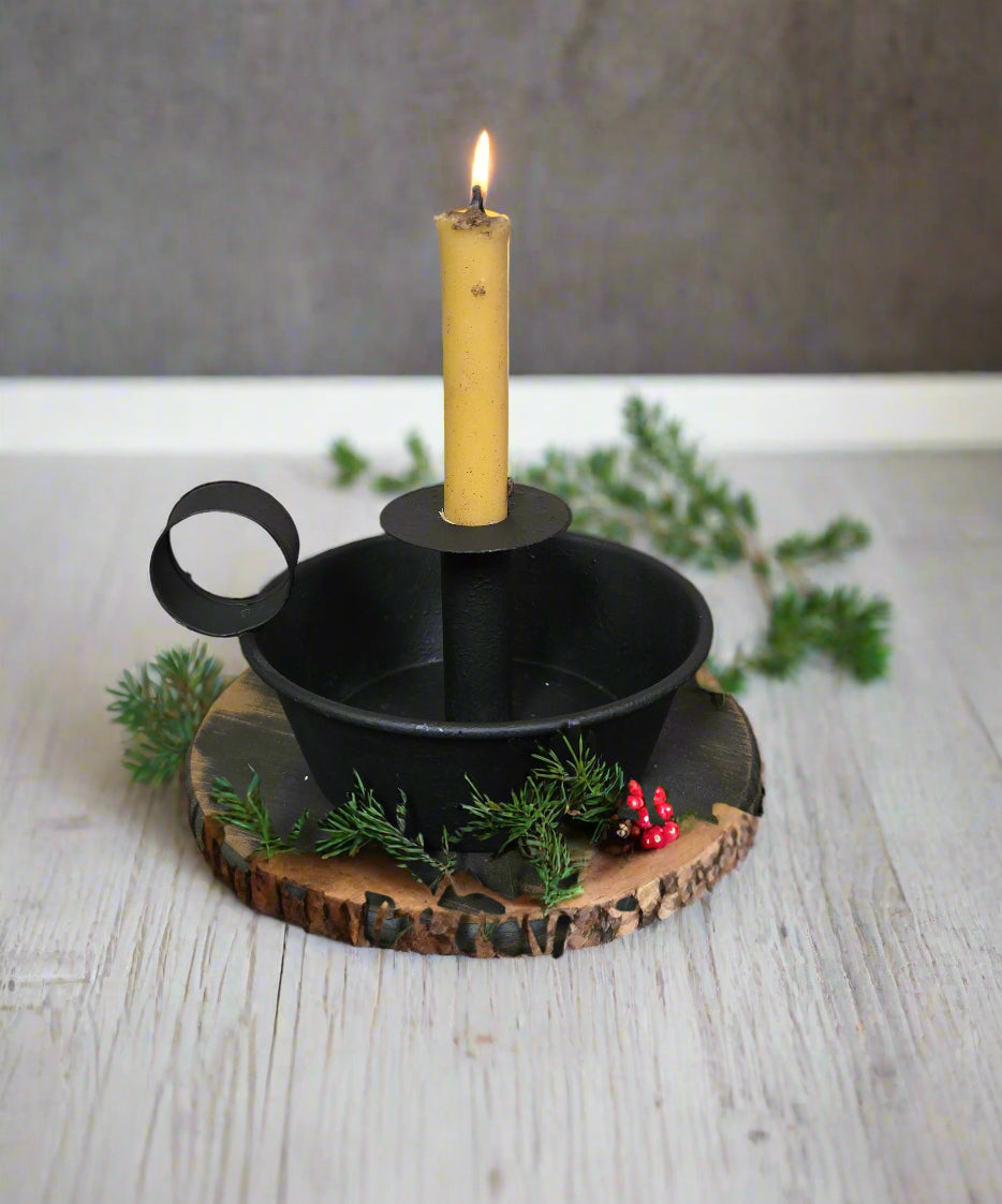 Deep dish candle holder with cream colored candle on a black riser among greenery