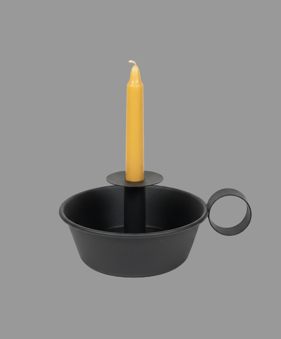 Deep dish candle holder with cream colored candle on a black riser among greenery