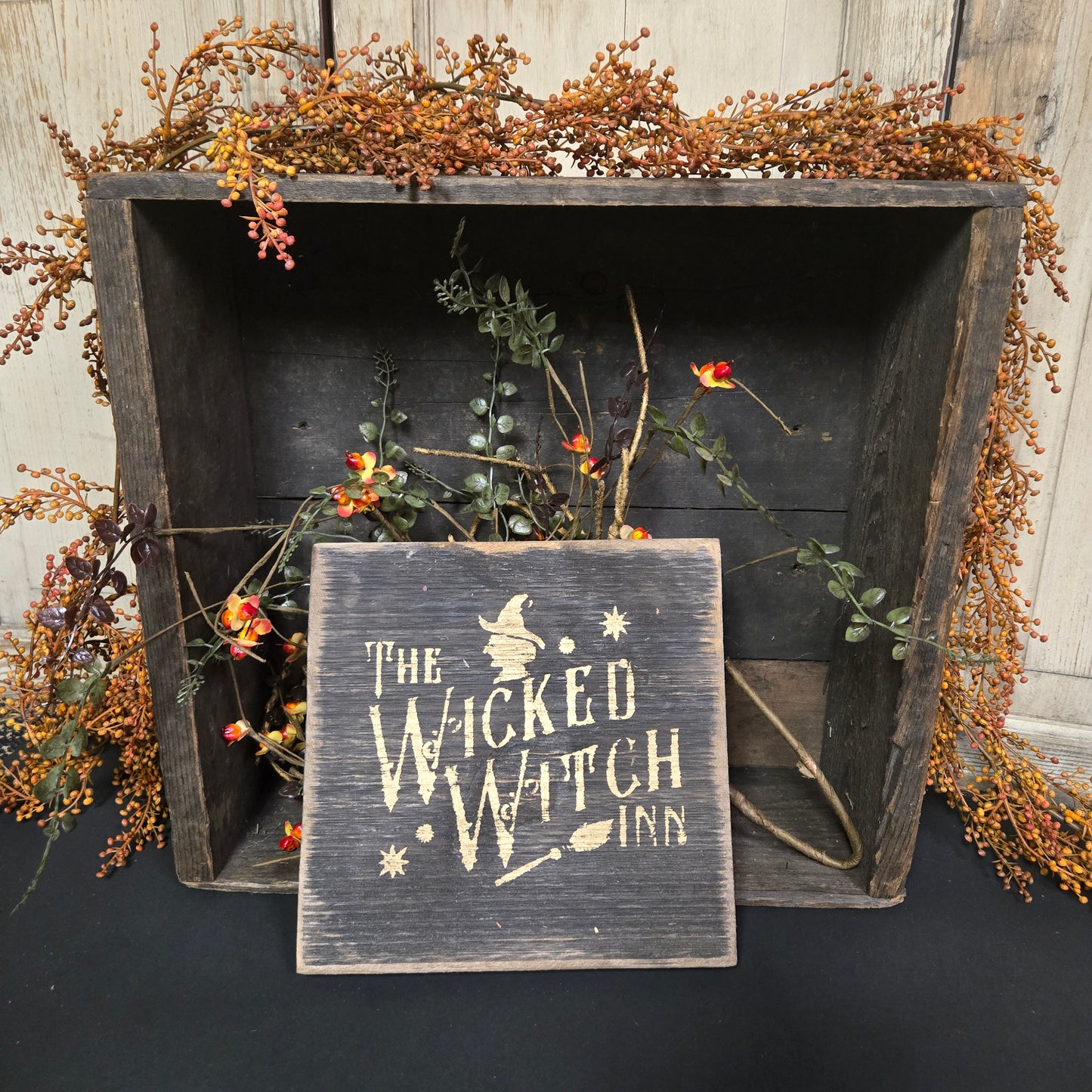 Wooden box with dried flowers and a sign reading 'The Wicked Witch' on a dark background.