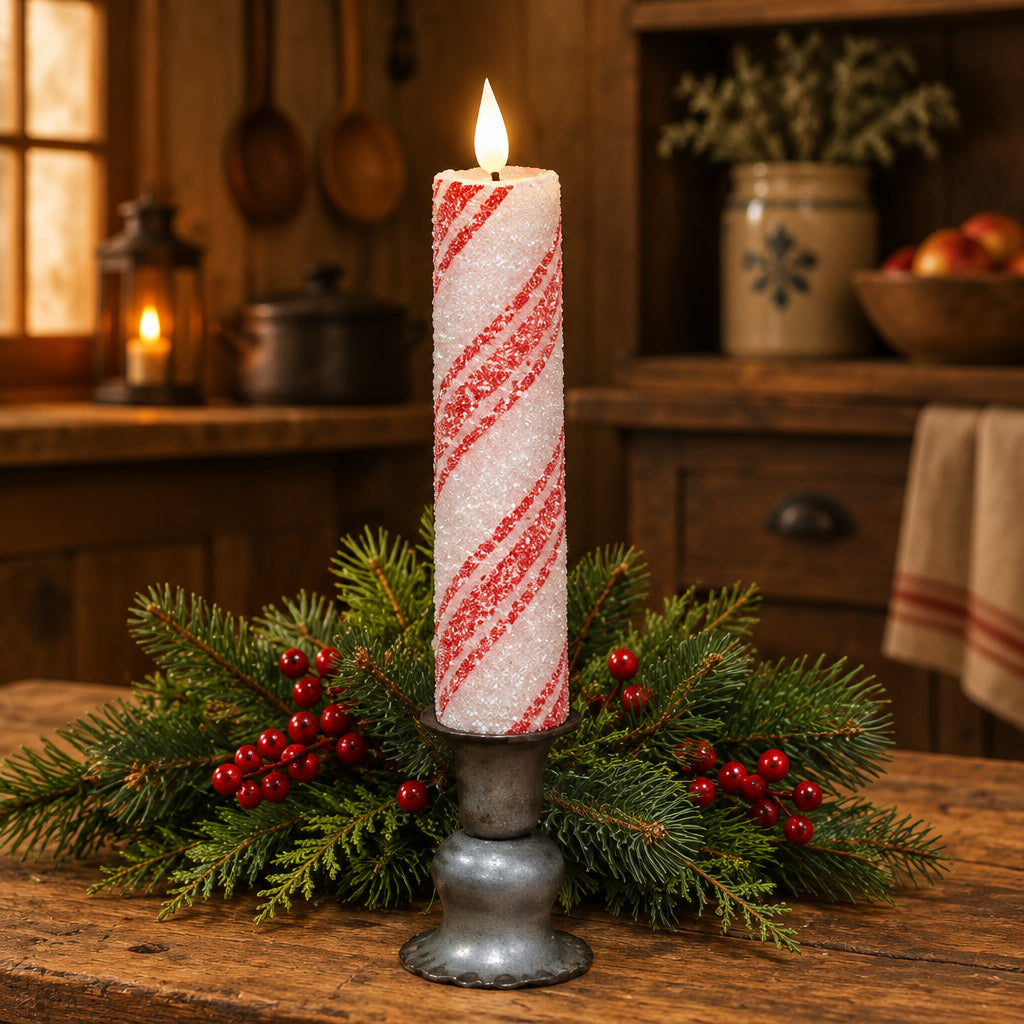 A LED taper candle with thick glittered candy cane design, placed on a wooden surface with pine branches in the background.