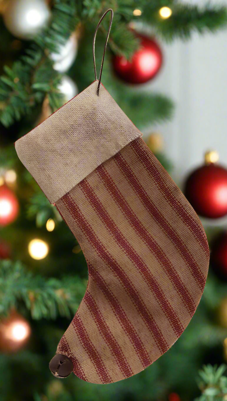 A rustic fabric holiday stocking with a ticking stripe pattern, featuring an antique white fabric cuff and a rusty jingle bell.