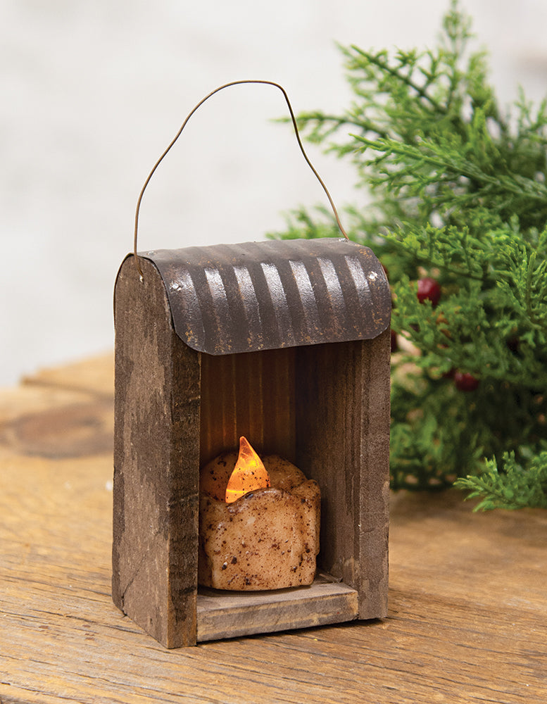 Tin roof tealight hut ornament holding battery operated tealight on wood surface with greenery in background