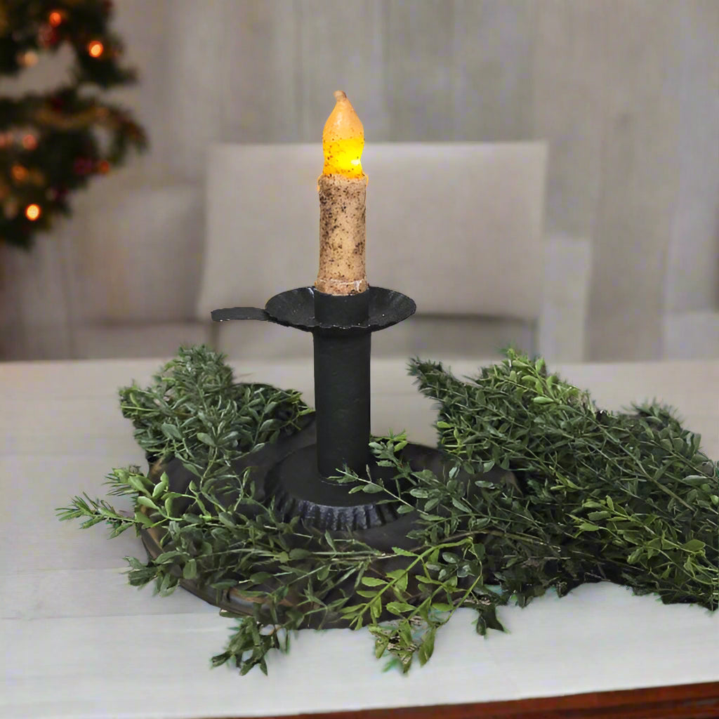 Textured black candlestick on a table with greenery around it