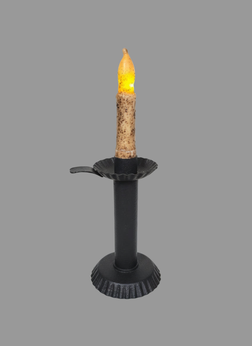 Textured black candlestick on a table with greenery around it