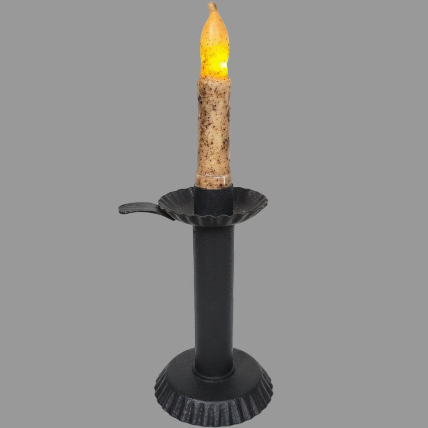 Textured black candlestick on a table with greenery around it