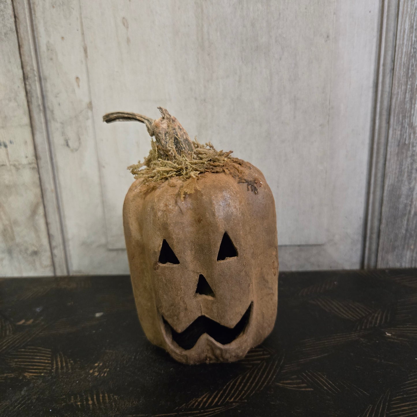Worn-out pumpkin lantern with jack-o'-lantern face on a textured wall.