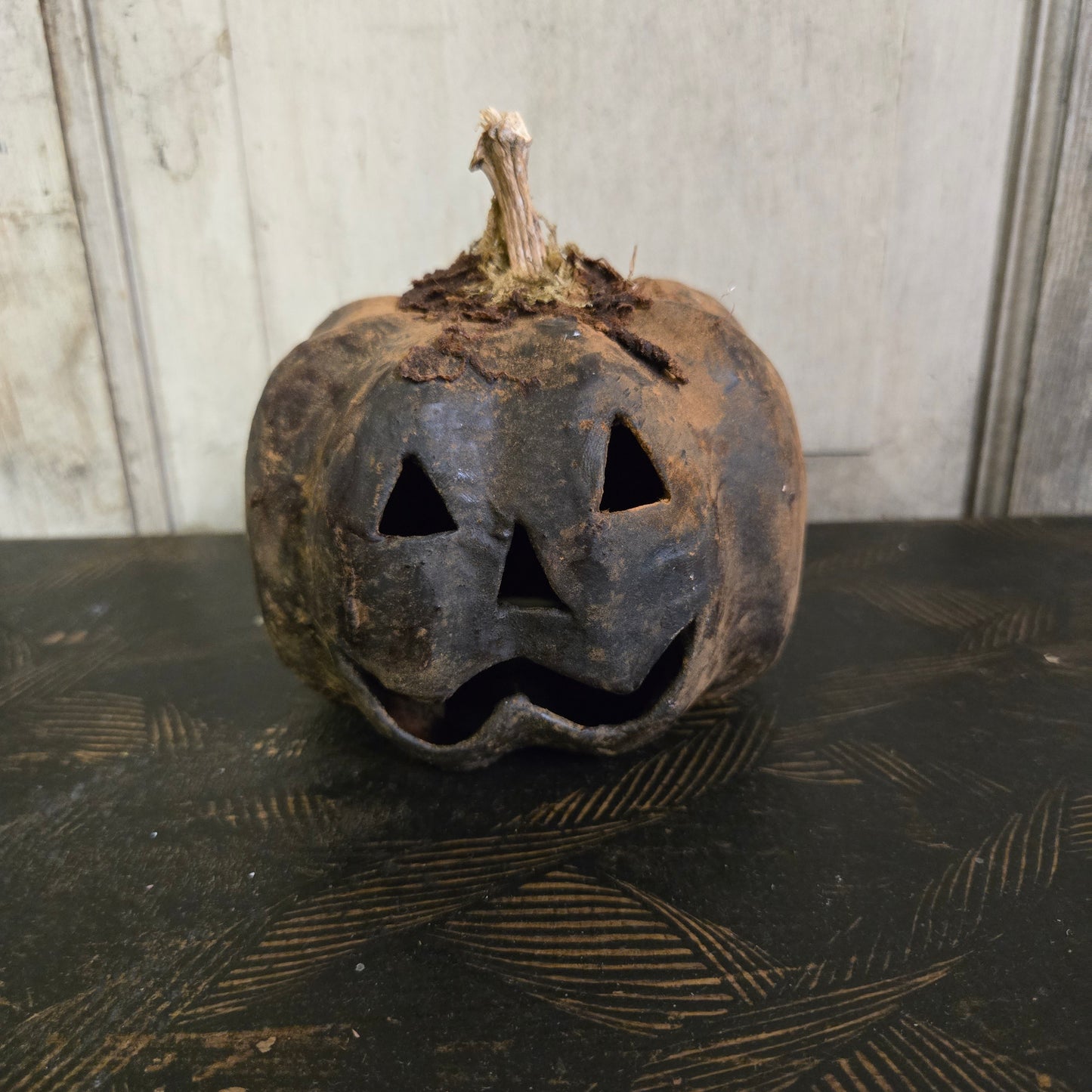 Worn-out pumpkin with a jack-o'-lantern face against a textured wall.