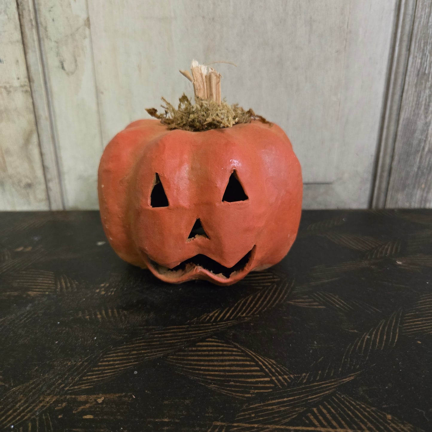 Small carved pumpkin leaning against a textured wall.
