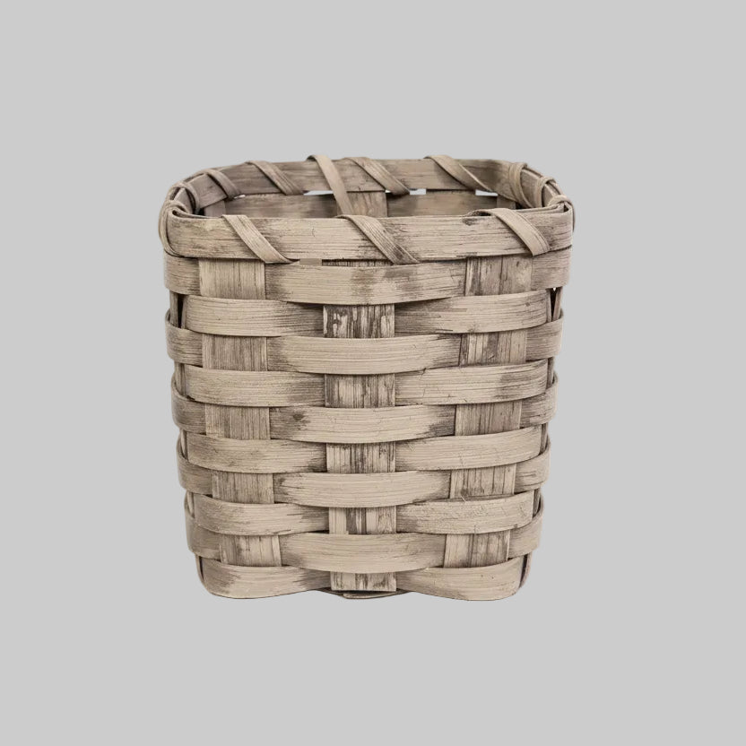 A beige wicker tissue box holder placed on a black patterned floor against a wooden backdrop.