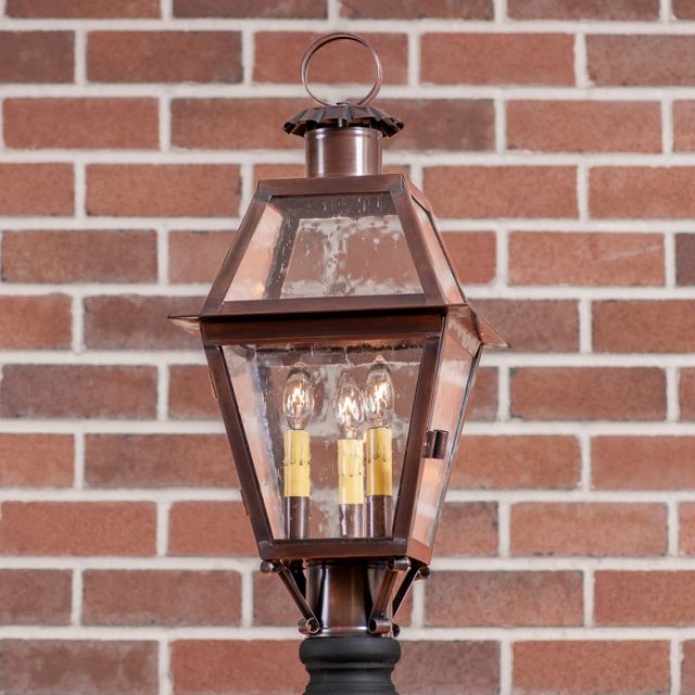 Decorative outdoor lamp with clear glass and brass finish against a brick wall.