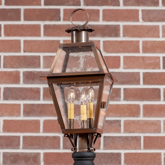 Decorative outdoor lamp with clear glass cover against a brick wall background