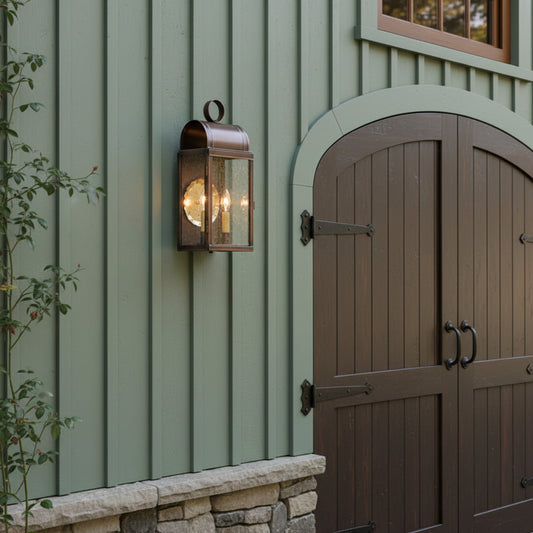A wall-mounted outdoor wall light with a solid antique copper finish, featuring a clear glass and two visible bulb sockets inside mounted on carriage house.