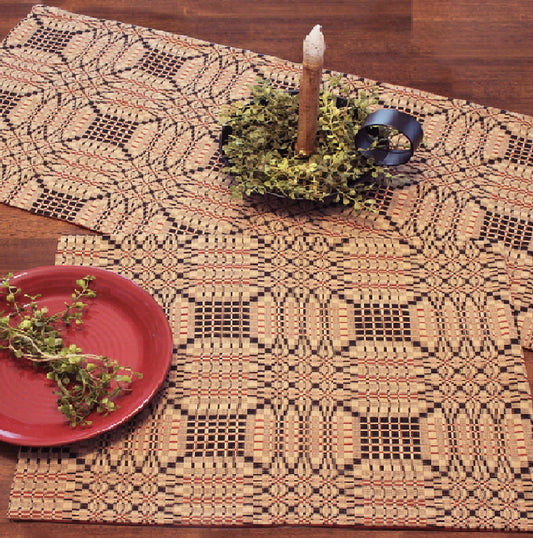 A jacquard placemat with a geometric pattern in black, red, and beige colors, displayed on a table with a red plate and a candle holder.