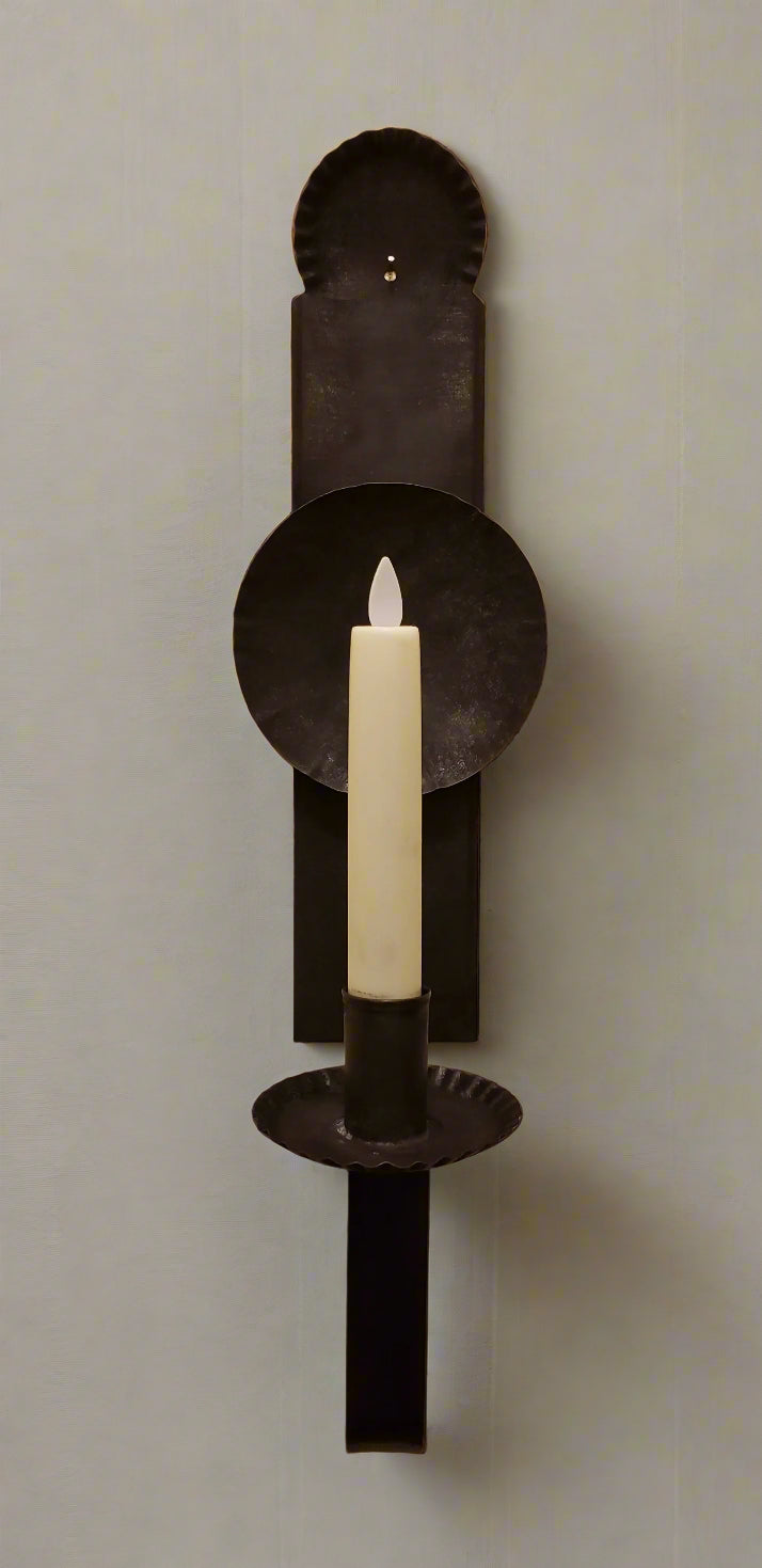 A black metal candle sconce with a primitive finish, hanging on a wall. It features a candle holder at the top.