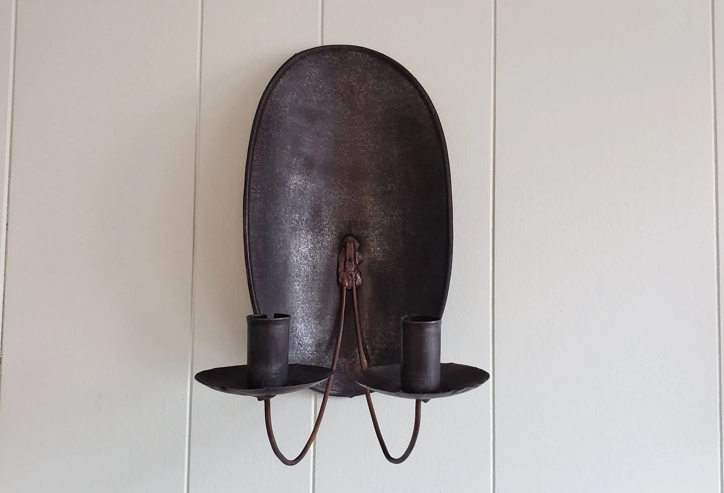 A brown metal turtleback tin candle sconce mounted on a wall, with two candle holders.