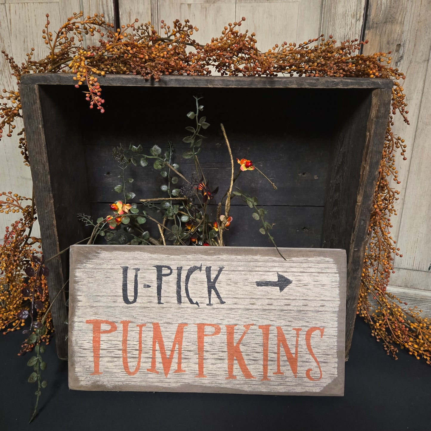 Wooden sign with 'U-Pick Pumpkins' text on a rustic wooden surface with foliage.
