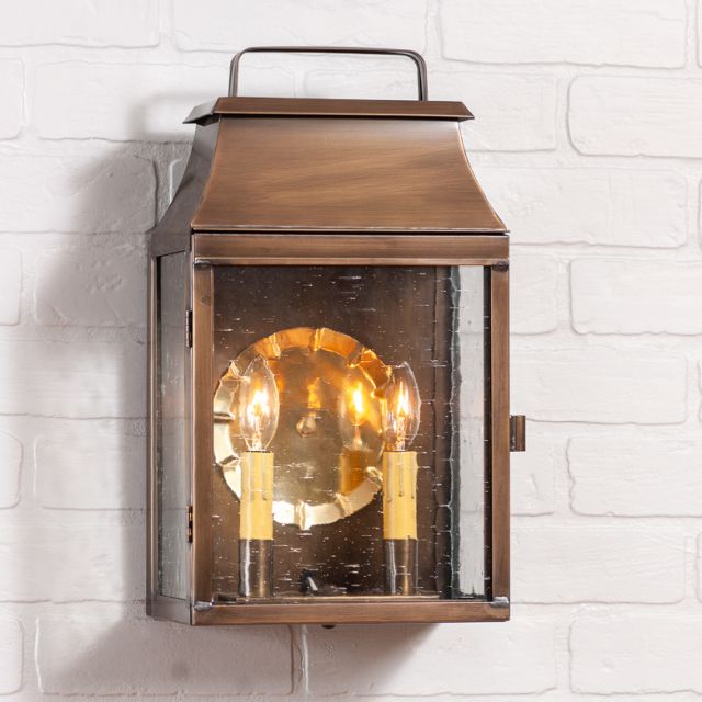 Colonial brass wall light with two candelabra bulbs and bubbly glass on a white brick wall.