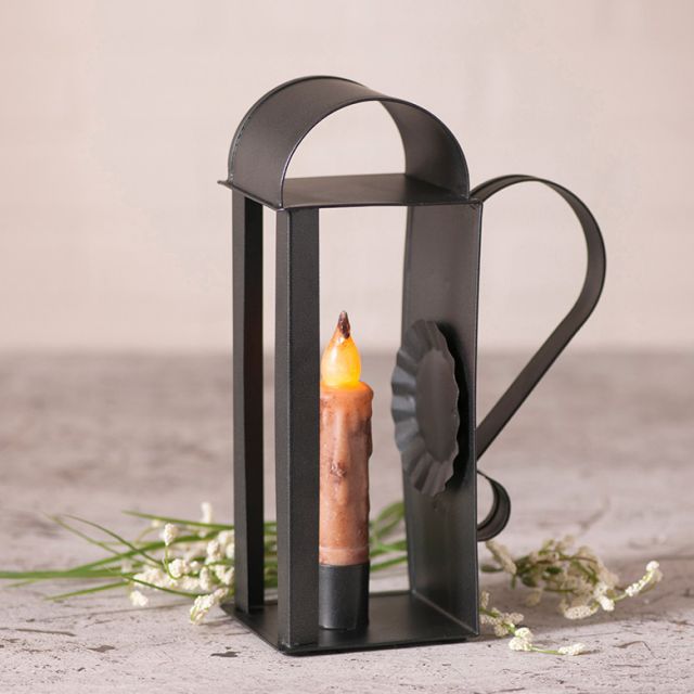 Tin candle holder that accommodates a real or battery operated taper candle with flowers in background.