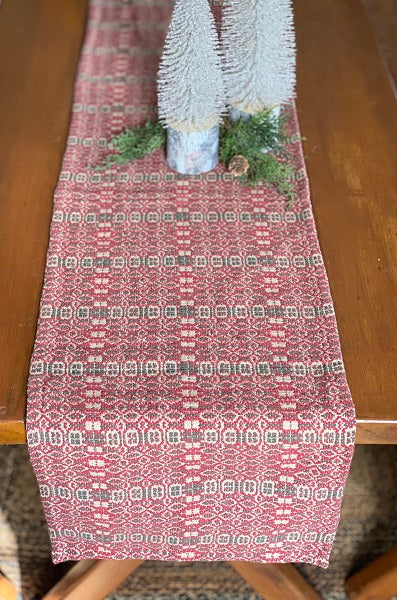 Decorative red and white patterned table runner with Christmas trees on a wooden table.