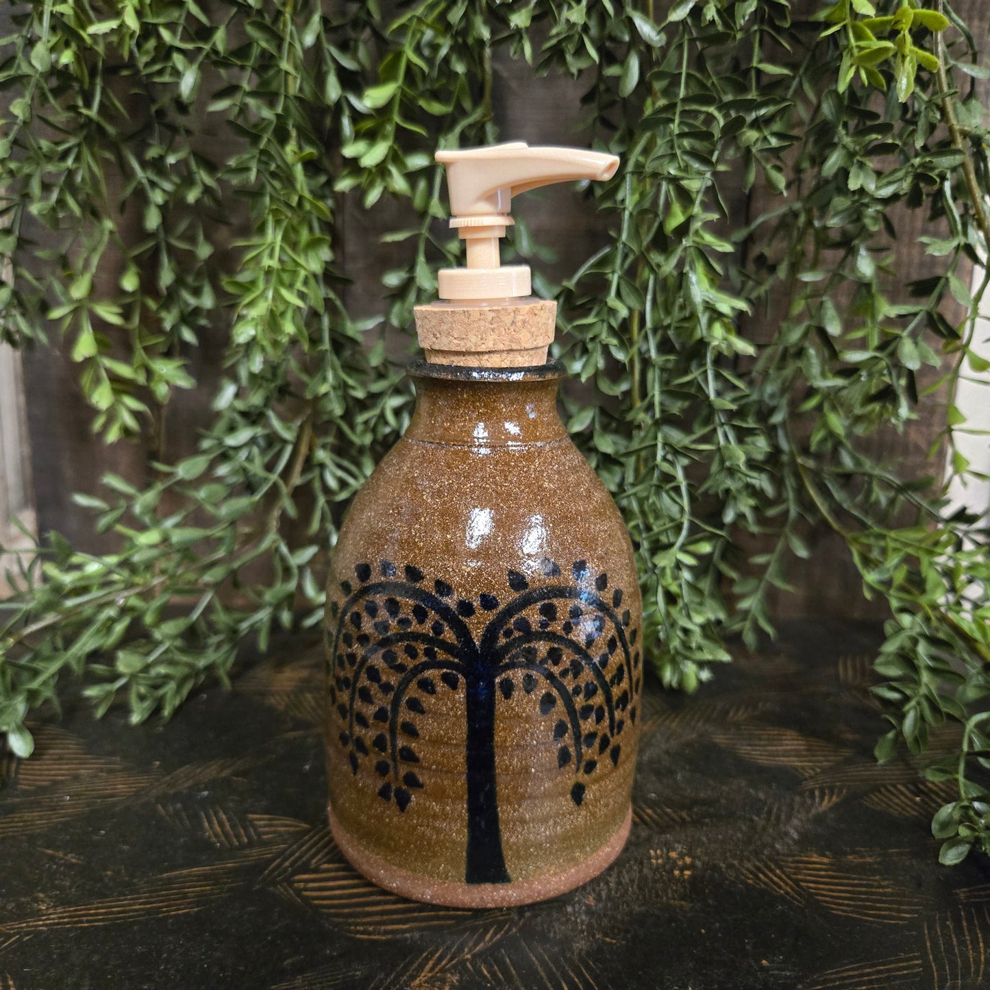 Decorative bottle with tree design on a wooden surface with greenery