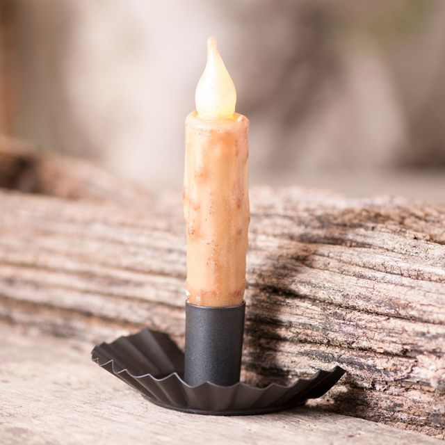 A beige candle placed in a smokey black metal candle holder, which is resting on a wooden surface.