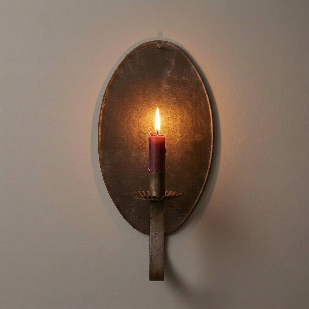 A brown tin candle sconce mounted on a wall, with a reflective surface and a hook for hanging candles.