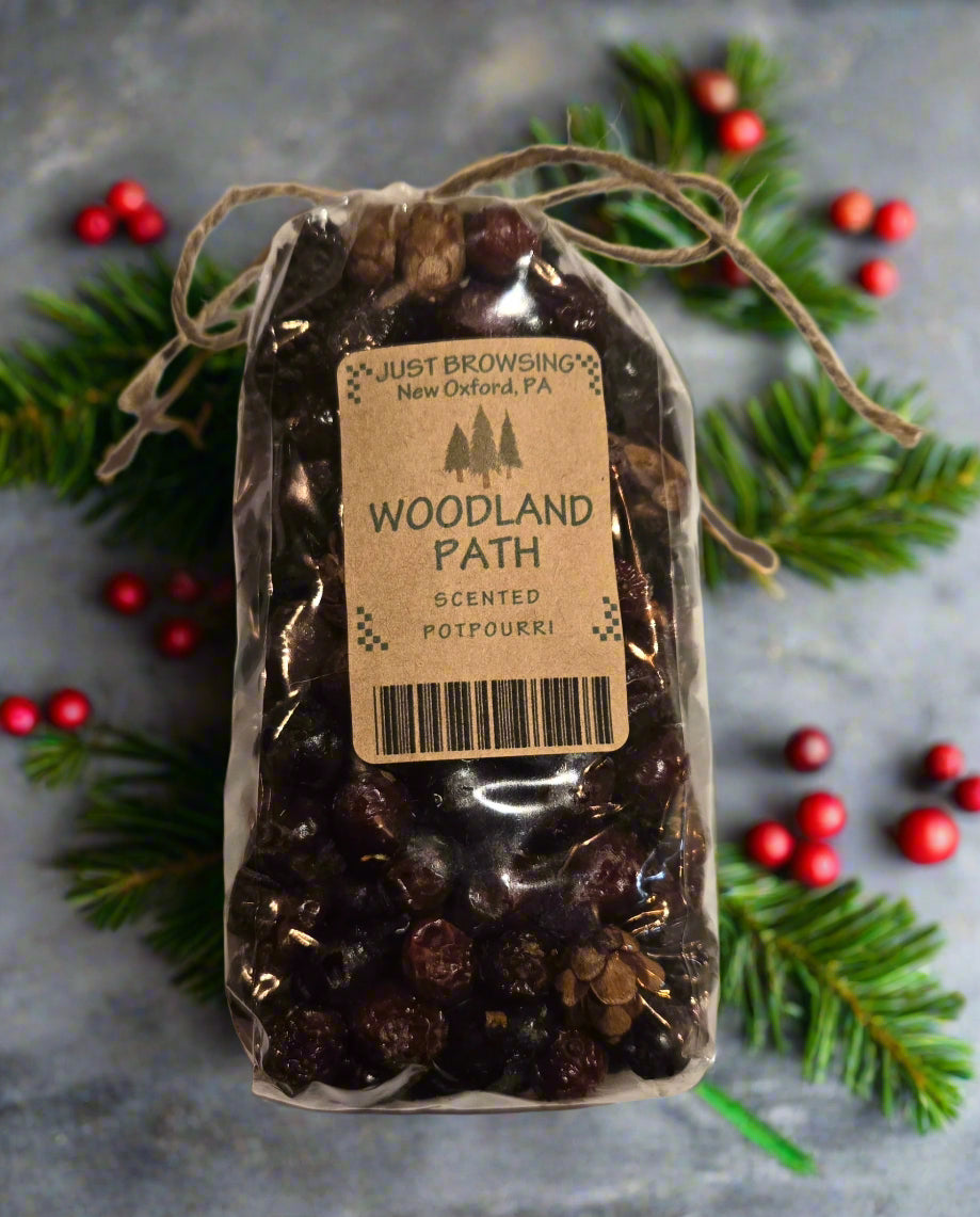 Packaged scented potpourri labeled 'Woodland Path' with Christmas decorations on a gray background