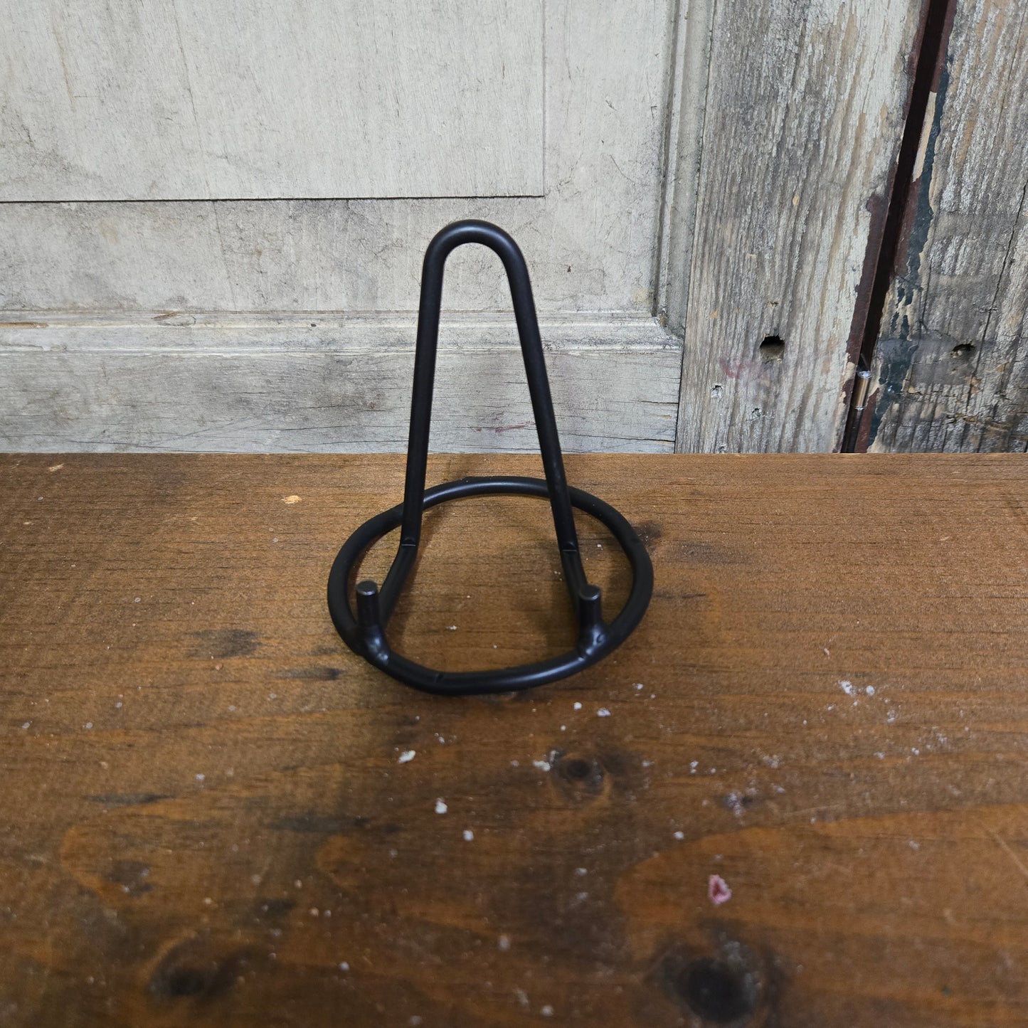 A wrought iron mini standing plate holder, black in color, placed on a wooden surface.