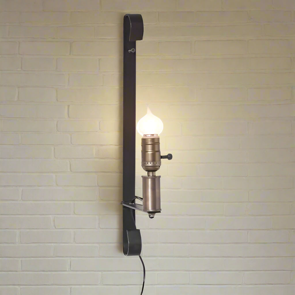 A wrought iron wall lamp with a black finish, featuring a hanging cord and a socket for a bulb.