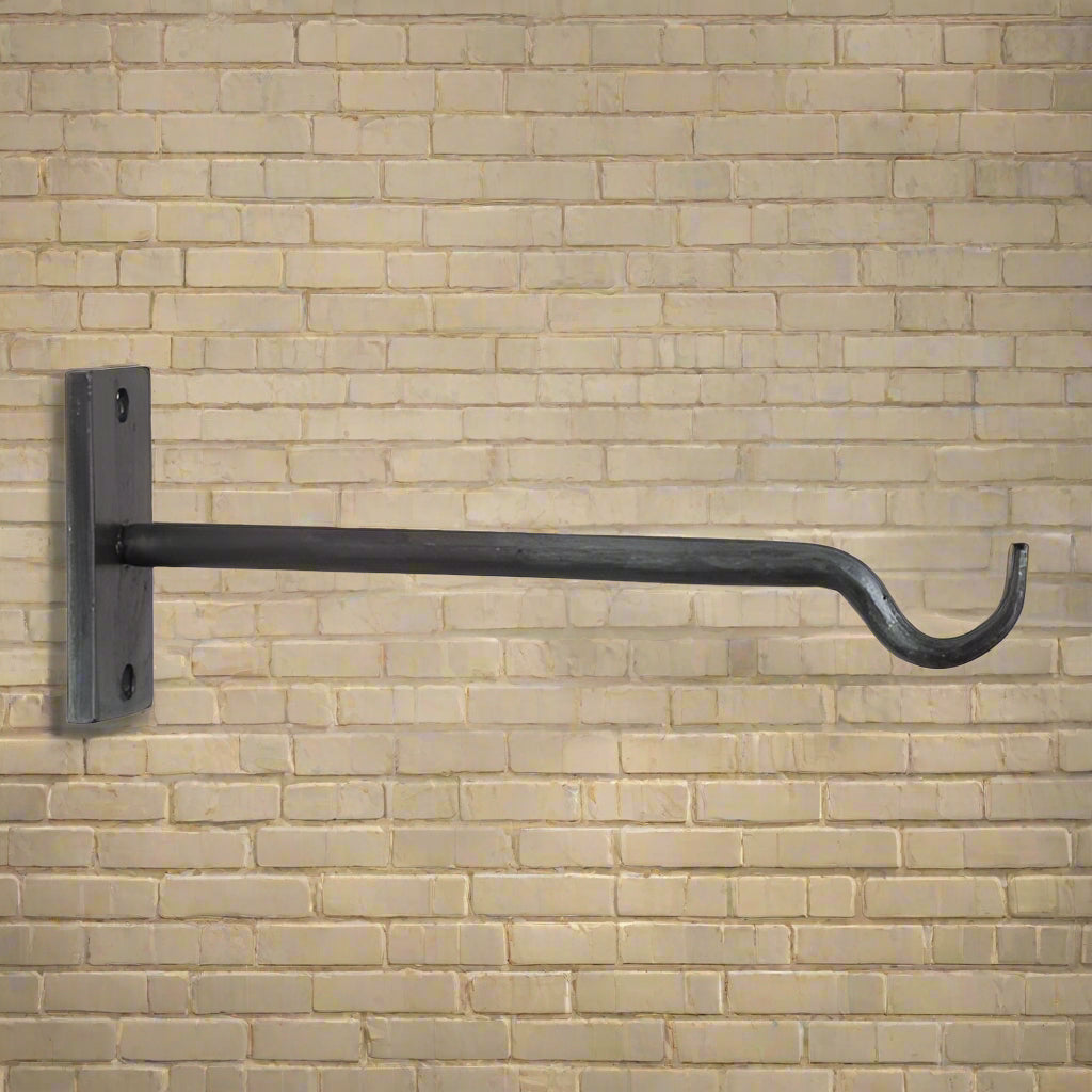 A wrought iron wall mounted plant hanger with an antique finish, featuring a curved hook and a horizontal bar, mounted on a plain wall.