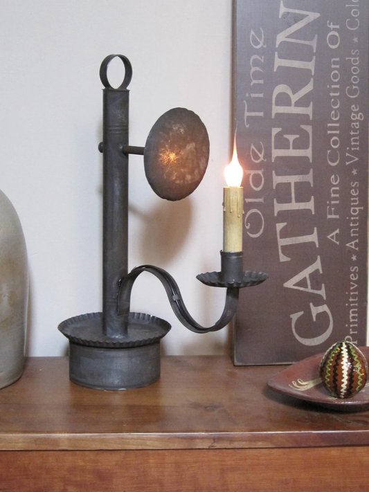 Decorative candle holder with a lit candle on a wooden surface, with a sign in the background.
