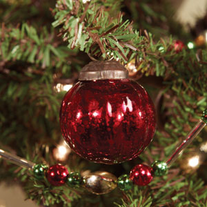 A red ridged glass ornament hanging from a Christmas tree, with a metallic cap at the top.