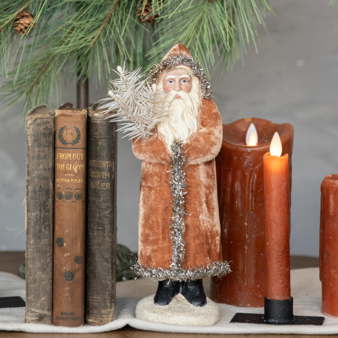 Decorative figure of a bearded man in a brown coat with candles and books on a table.