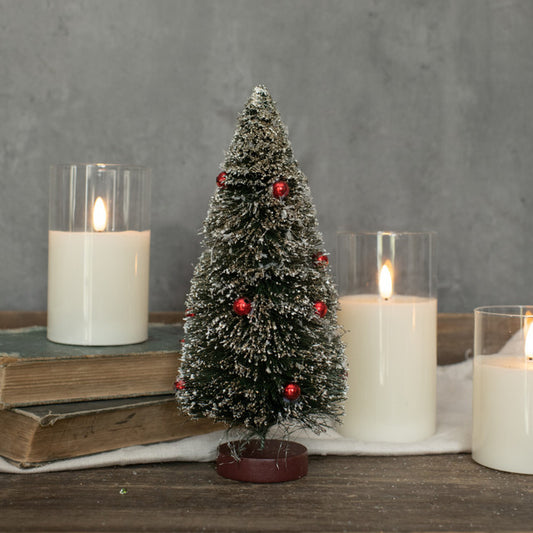 A small artificial green bottlebrush tree with red berries on a table, accompanied by candles and books.