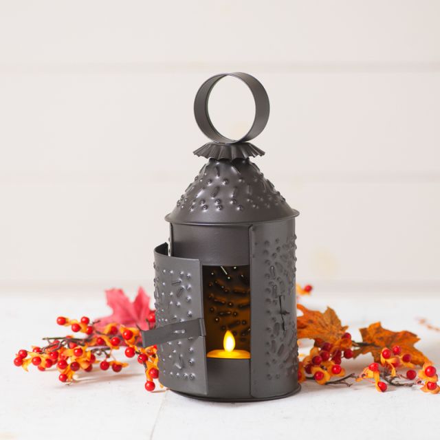 Tin lantern with tealight next to bittersweet on a white background.