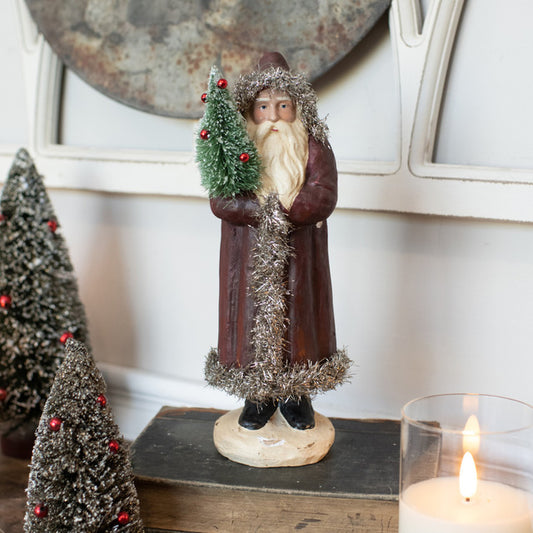 10 inch vintage belsnickel holding bottlebrush tree standing on a old book with candle and bottlebrush trees nearby.